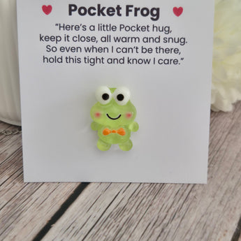 Green frog pocket hug token on a card with message, small keepsake for children, displayed on a wooden surface.